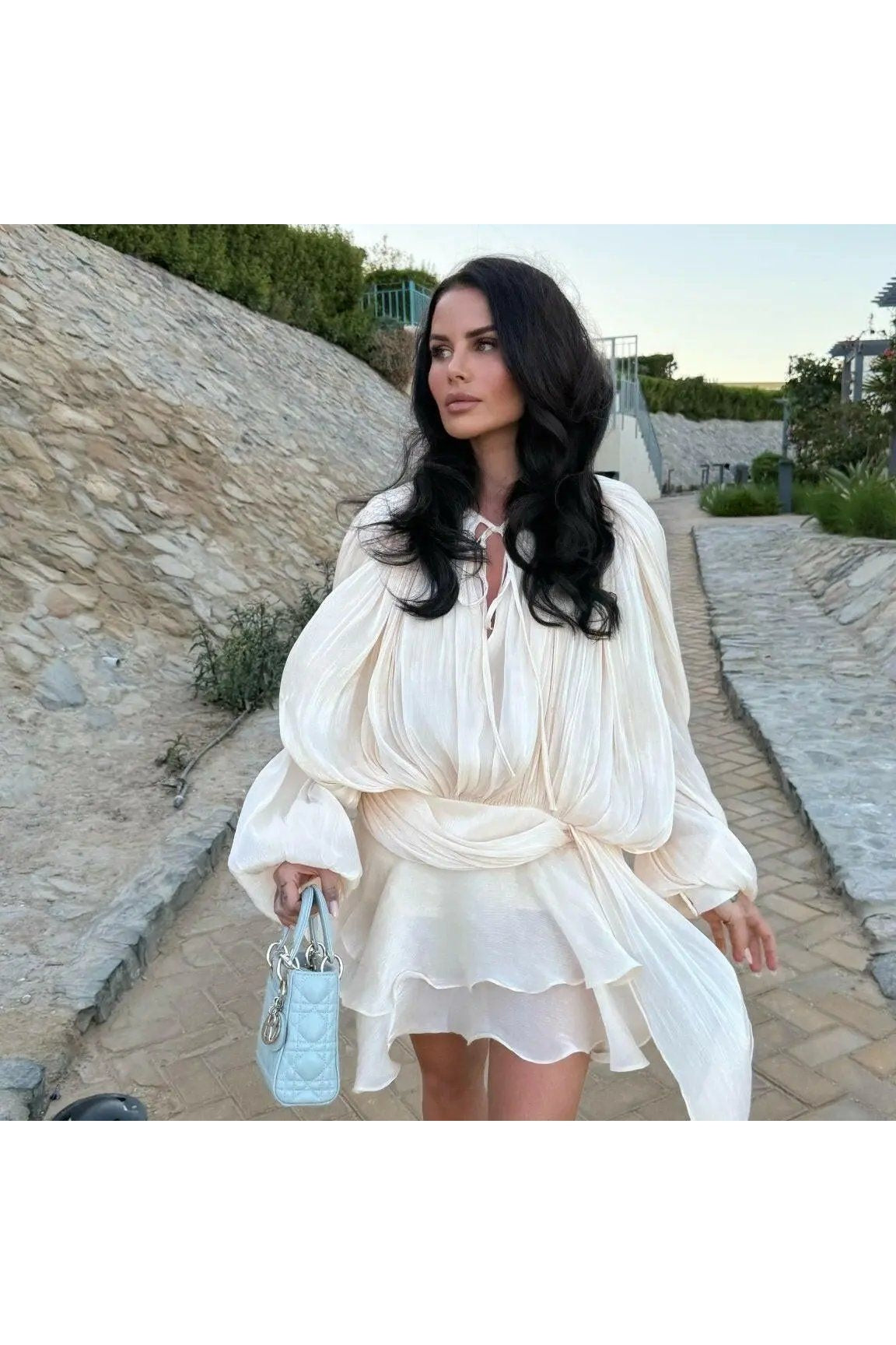 Model wearing Éloïse Plissee Kleid, showcasing elegant style with intricate design details on a stylish path.
