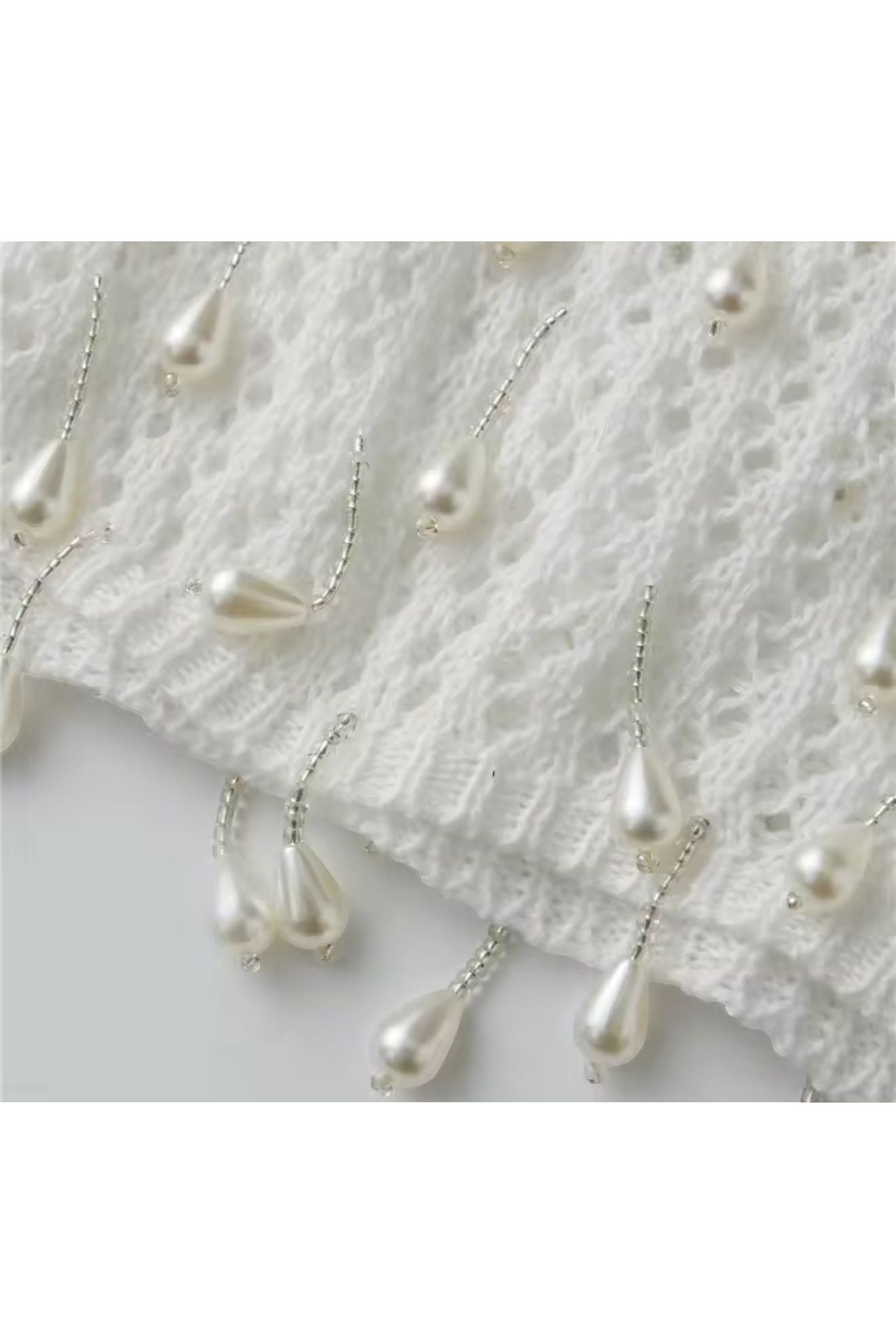 Miraee Paris white crochet cover-up featuring delicate hanging pearl-like teardrop embellishments on a knit fabric.