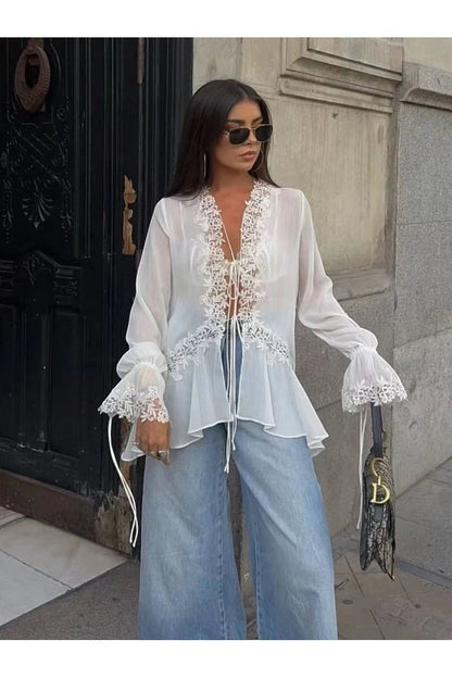 Miraee Paris white semi-transparent lace blouse with V-neck, tie-front, and ruffled sleeves worn with blue jeans.